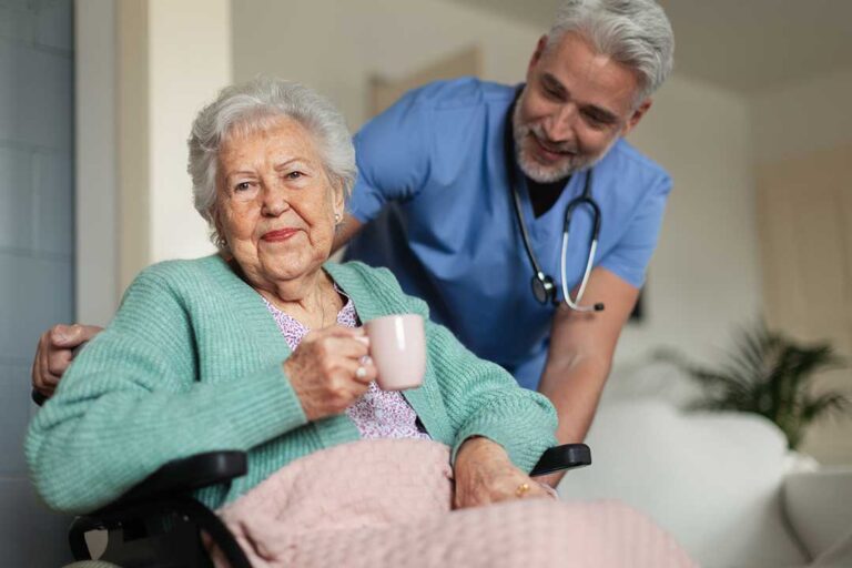 Caregiver assists an older resident in a bright assisted living common room.